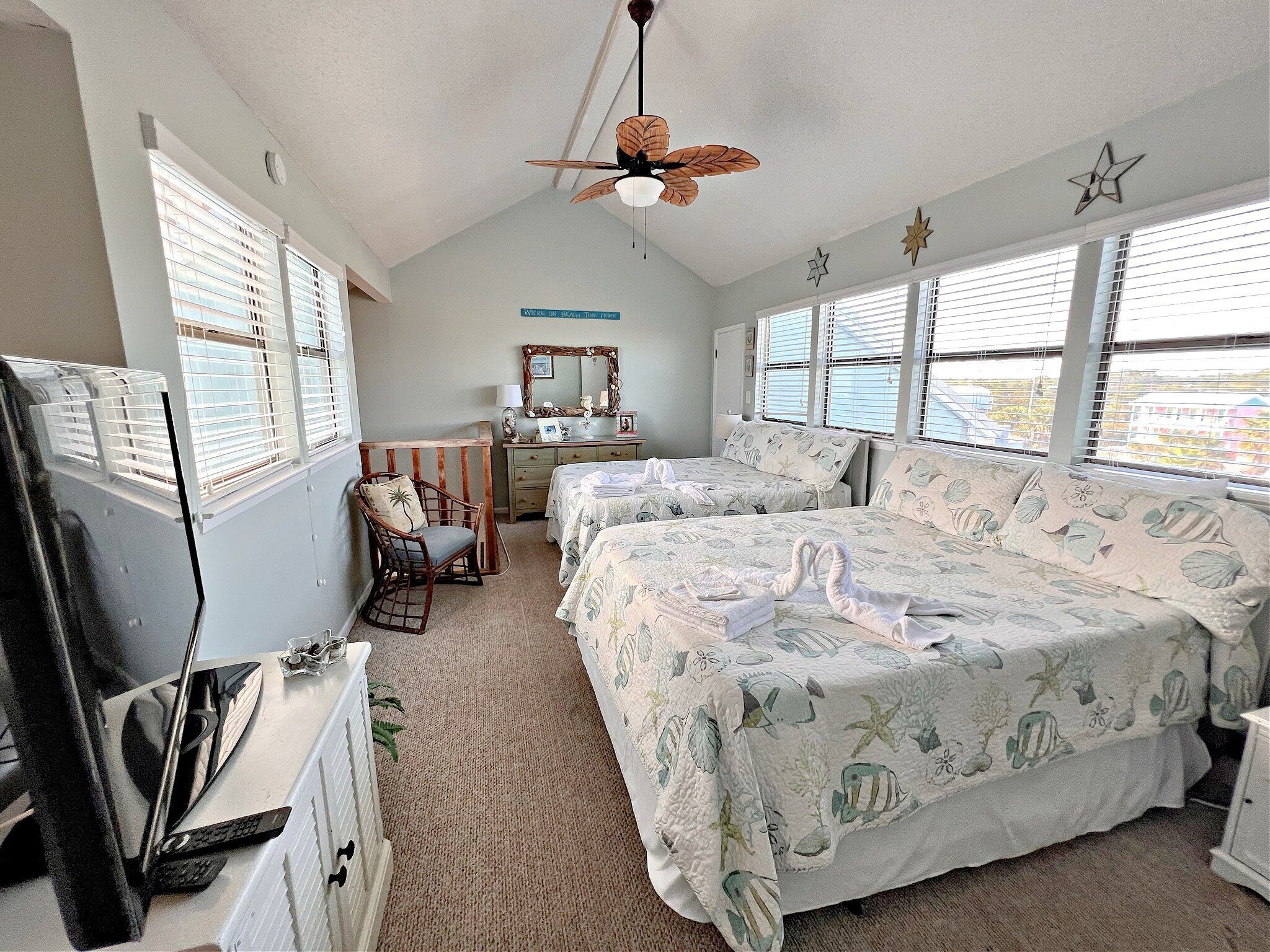 A bedroom with two beds, a desk, a chair, a TV, and a ceiling fan.