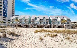 A beachfront hotel with multiple-story buildings, balconies, and a sandy beach in the foreground.