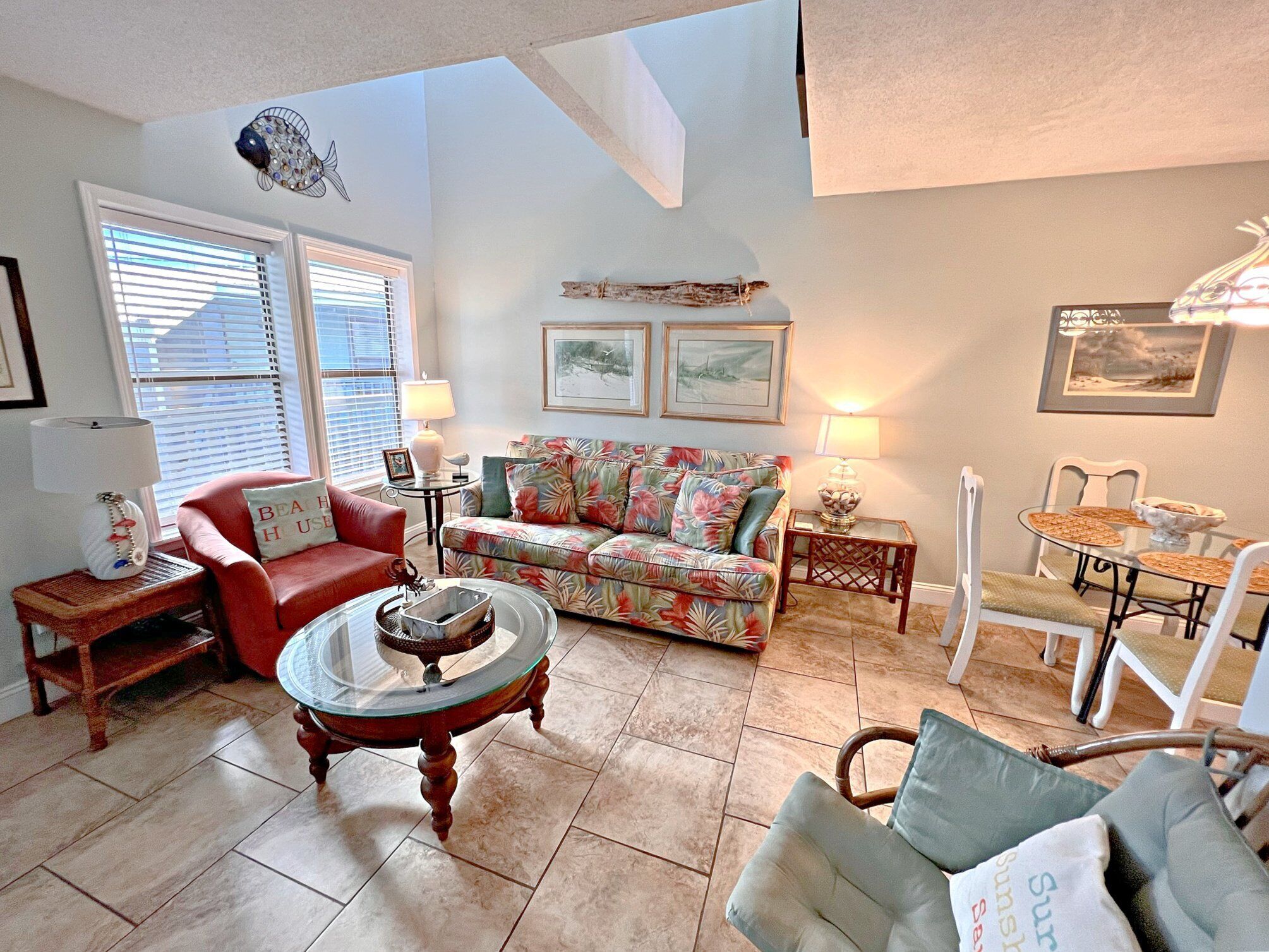 A living room with a red sofa, a floral couch, a glass coffee table, and a dining area with a glass table and white chairs.