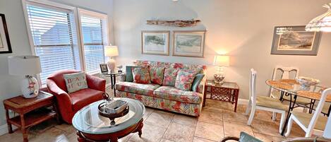A living room with a red sofa, a floral couch, a glass coffee table, and a dining area with a glass table and white chairs.