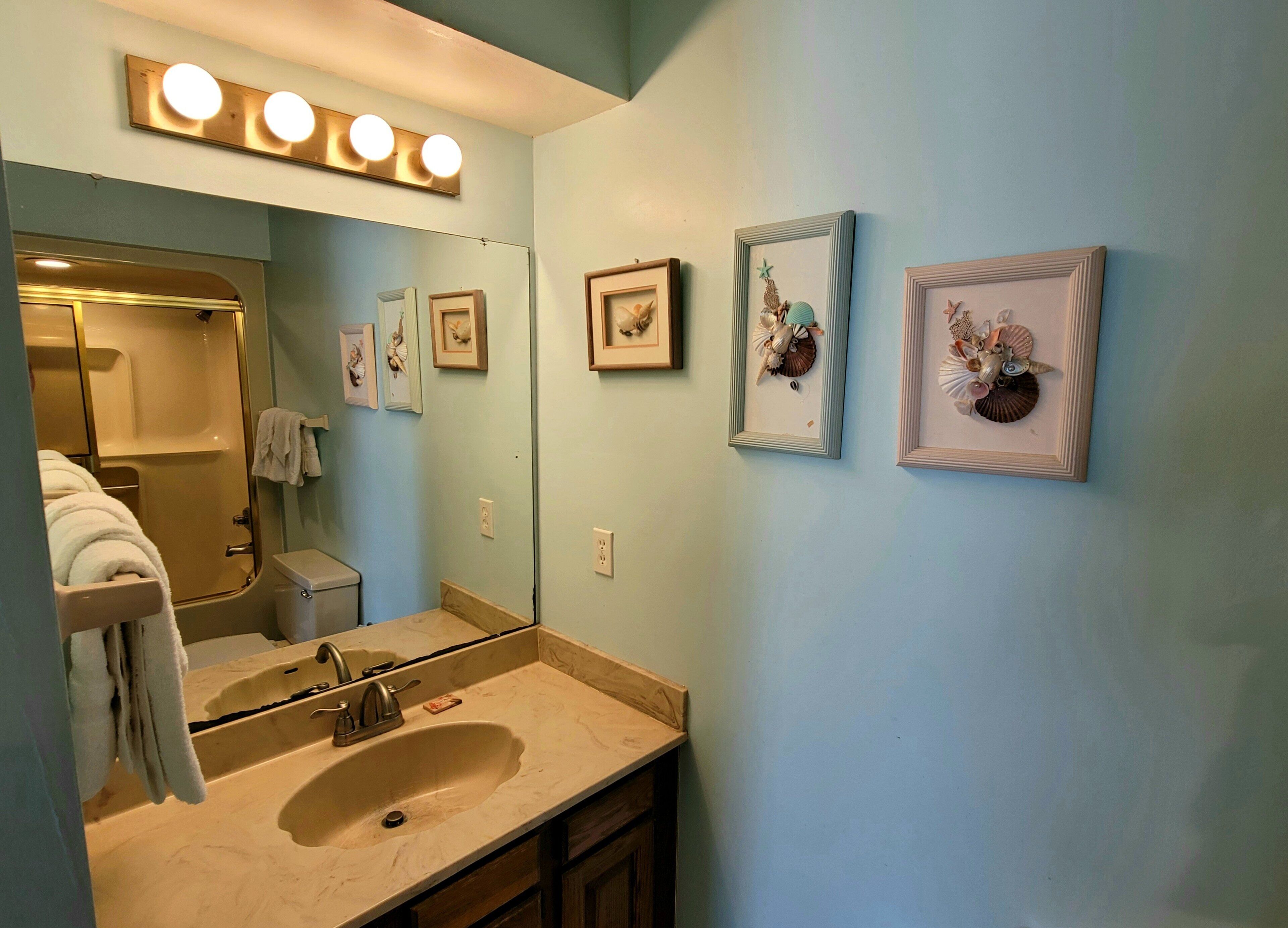 Un baño con lavamanos, espejo y una obra de arte enmarcada en la pared.