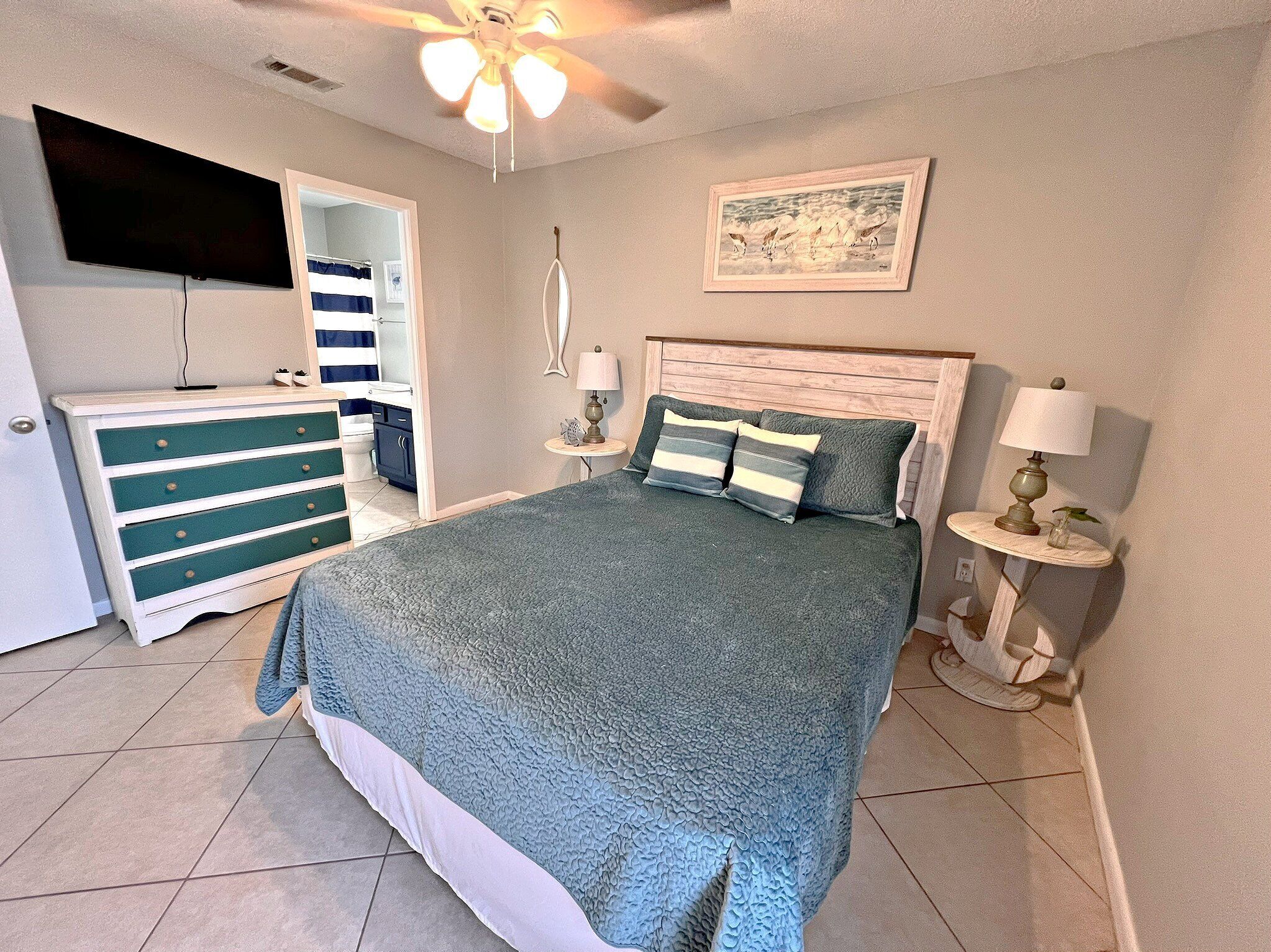 Un dormitorio con cama, cómoda, televisor y ventilador de techo.