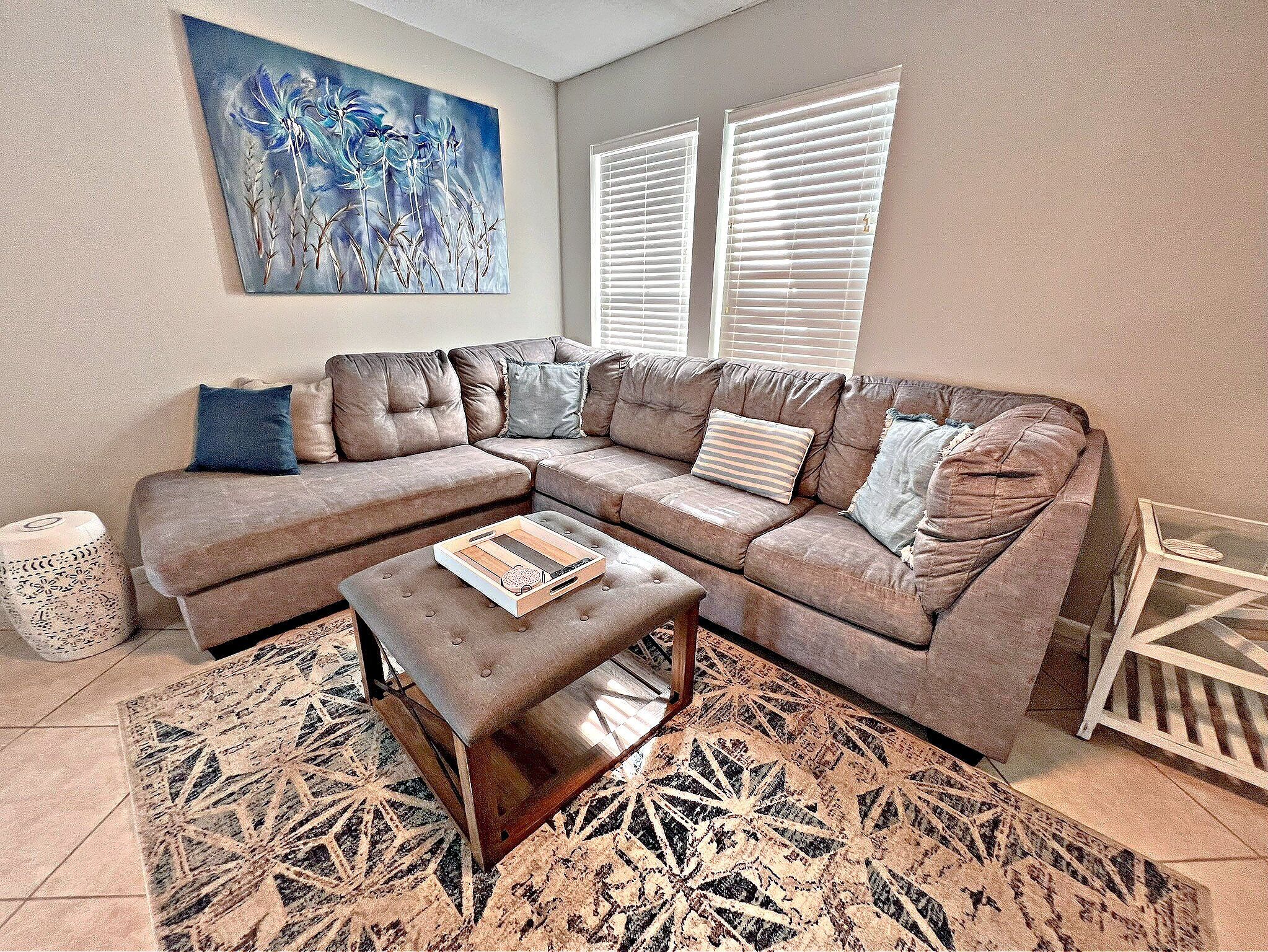 A living room with a sectional sofa, a coffee table, a patterned rug, and a painting on the wall.