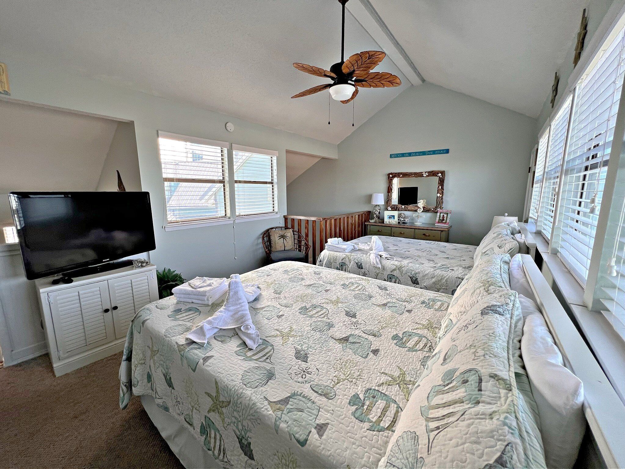 A bedroom with two beds, a TV, a ceiling fan, and a window with blinds.