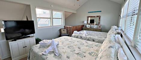 Un dormitorio con dos camas, televisión, ventilador de techo y ventana con persianas.