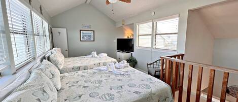 A bedroom with two beds, a ceiling fan, a TV, and a balcony.