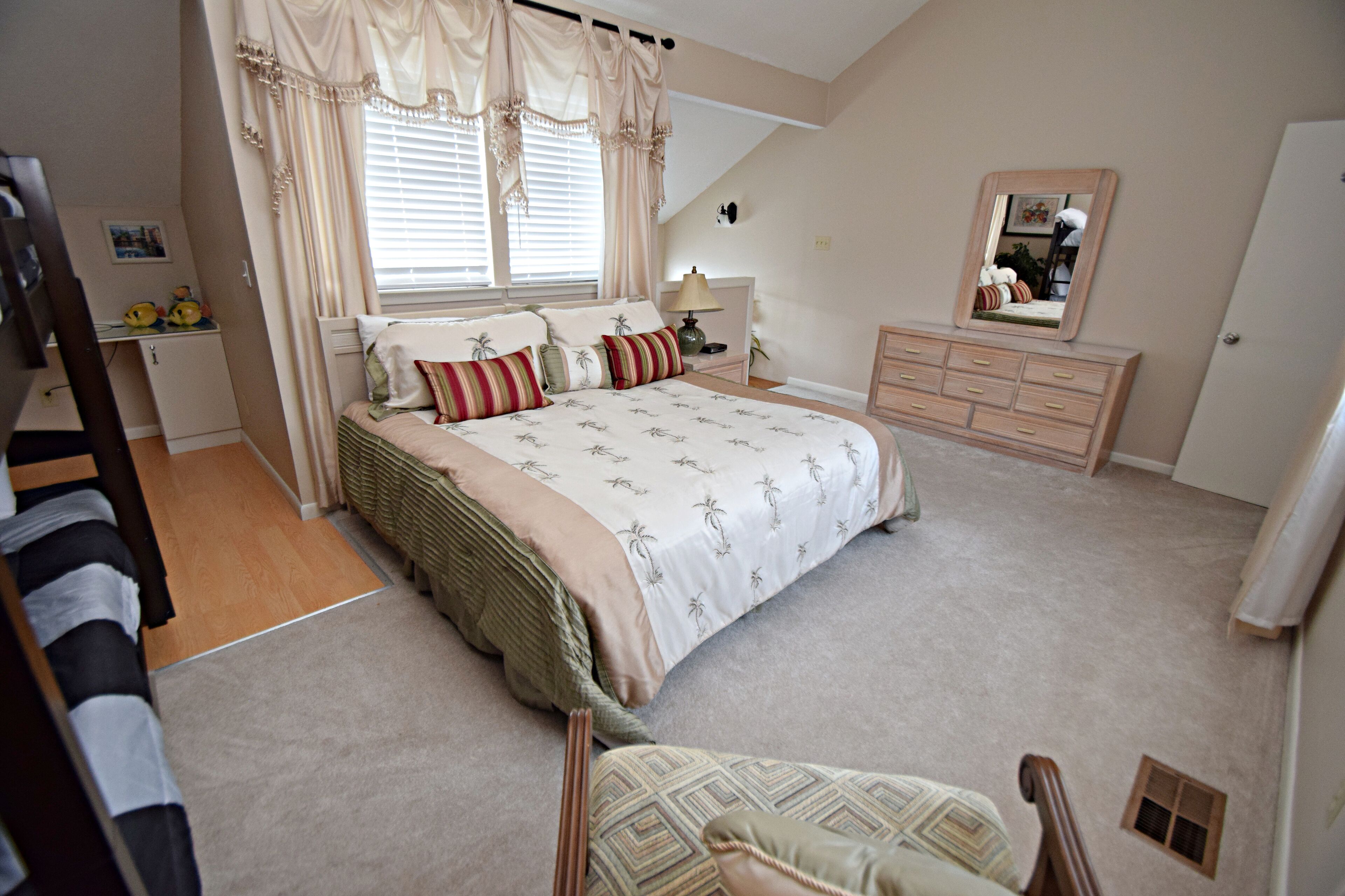 A bedroom with a bed, dresser, mirror, and a desk with a lamp.