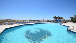 A swimming pool with clear blue water, surrounded by blue lounge chairs and a palm tree. - Phoenix East (Orange Beach)