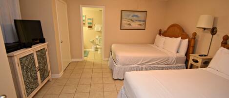A hotel room with two beds, a television on a cabinet, a ceiling fan, and a painting on the wall.
