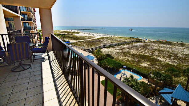 A balcony with a view of a beach, a pool, and a building with multiple floors. - Phoenix East (Orange Beach)