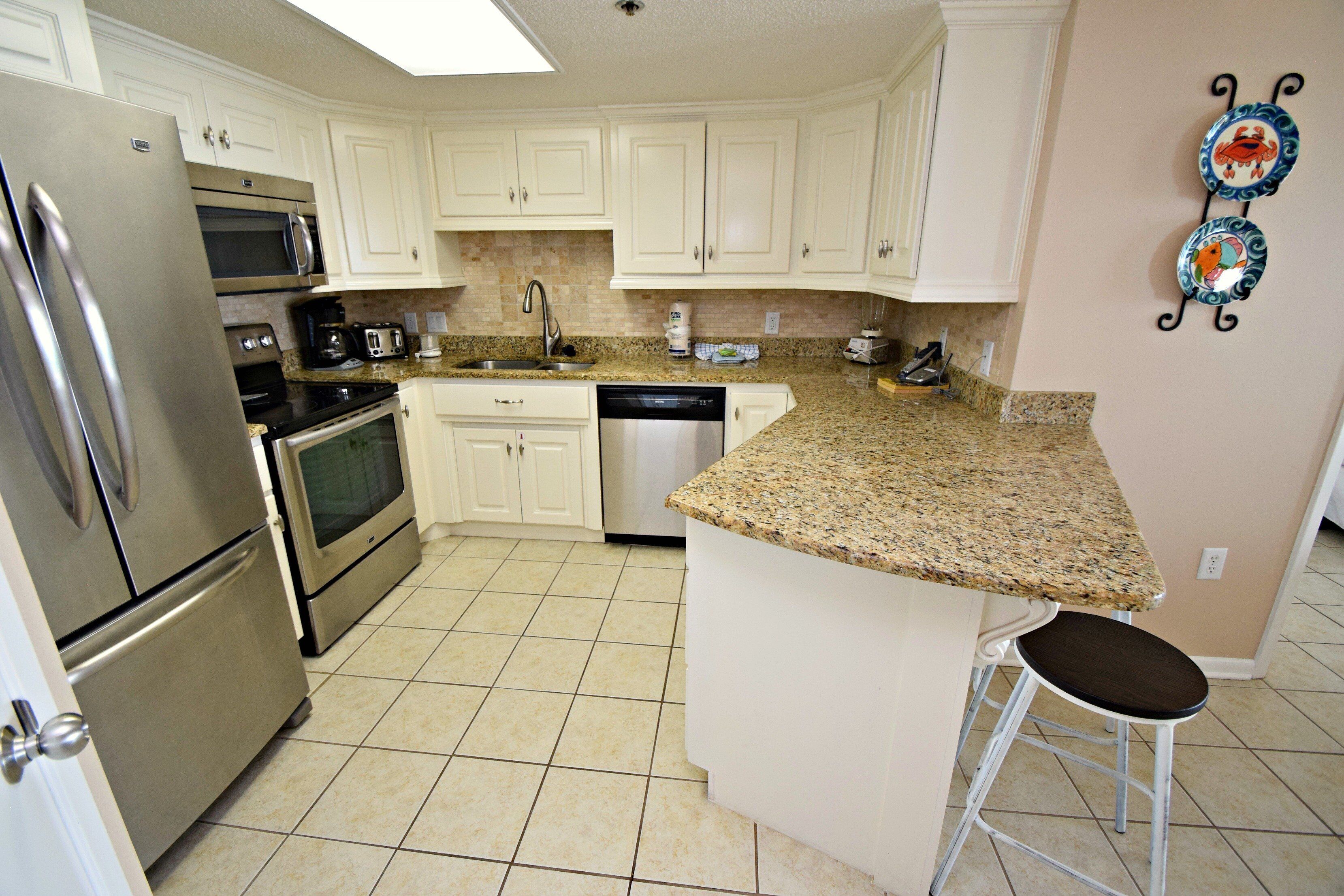 A kitchen with white cabinets, stainless steel appliances, a granite countertop, and a bar stool.