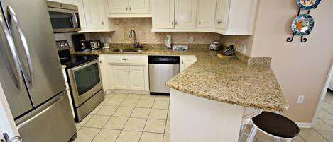 A kitchen with white cabinets, stainless steel appliances, a granite countertop, and a bar stool.