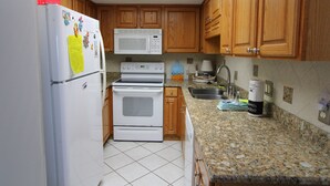 A kitchen with wooden cabinets, a white refrigerator, a microwave, an oven, a sink, and a granite countertop. - Phoenix II (Orange Beach)