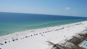 A beach with umbrellas and people, a clear sky, and a pool area. - Phoenix II (Orange Beach)