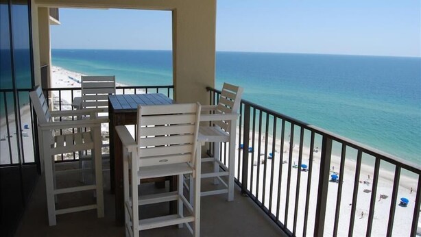 A balcony with white chairs and a table, overlooking a beach with clear blue water and a sandy shore. - Phoenix II (Orange Beach)