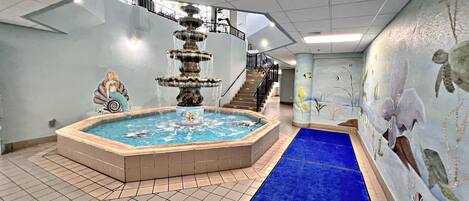 Una piscina con una fuente, suelo de baldosas y una alfombra azul que lleva a una escalera.