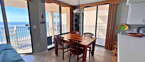 A spacious living area with a wooden dining table and chairs, a blue sofa, and a view of the ocean through large sliding glass doors.