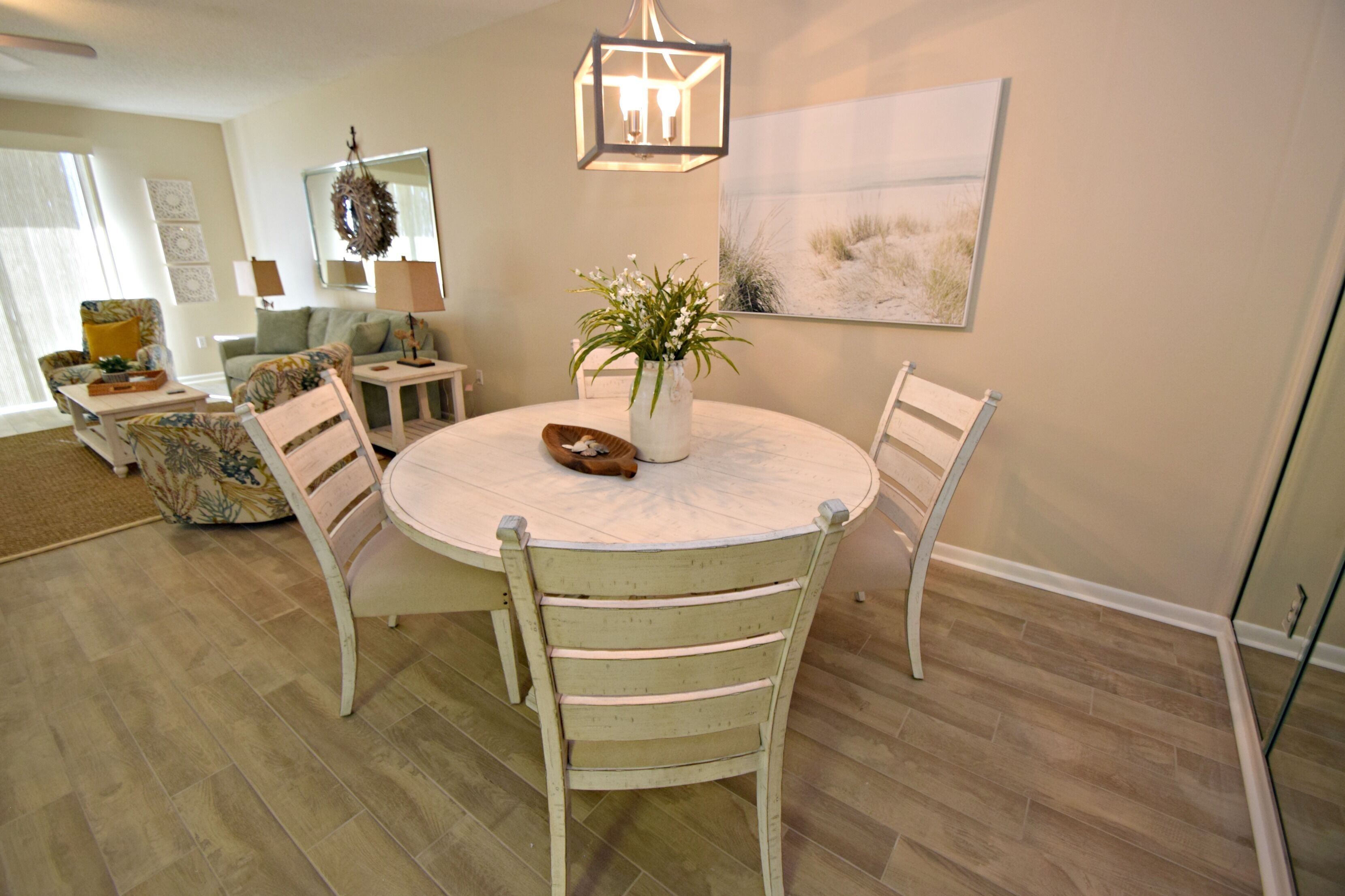 A dining area with a round table, four chairs, a vase with flowers, and a hanging light fixture.