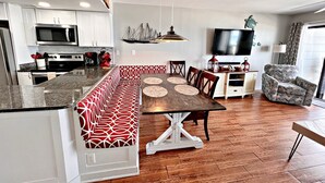 A modern kitchen with white cabinets, a built-in microwave, and a large island with a red and white patterned bench. - Regatta (Gulf Shores)