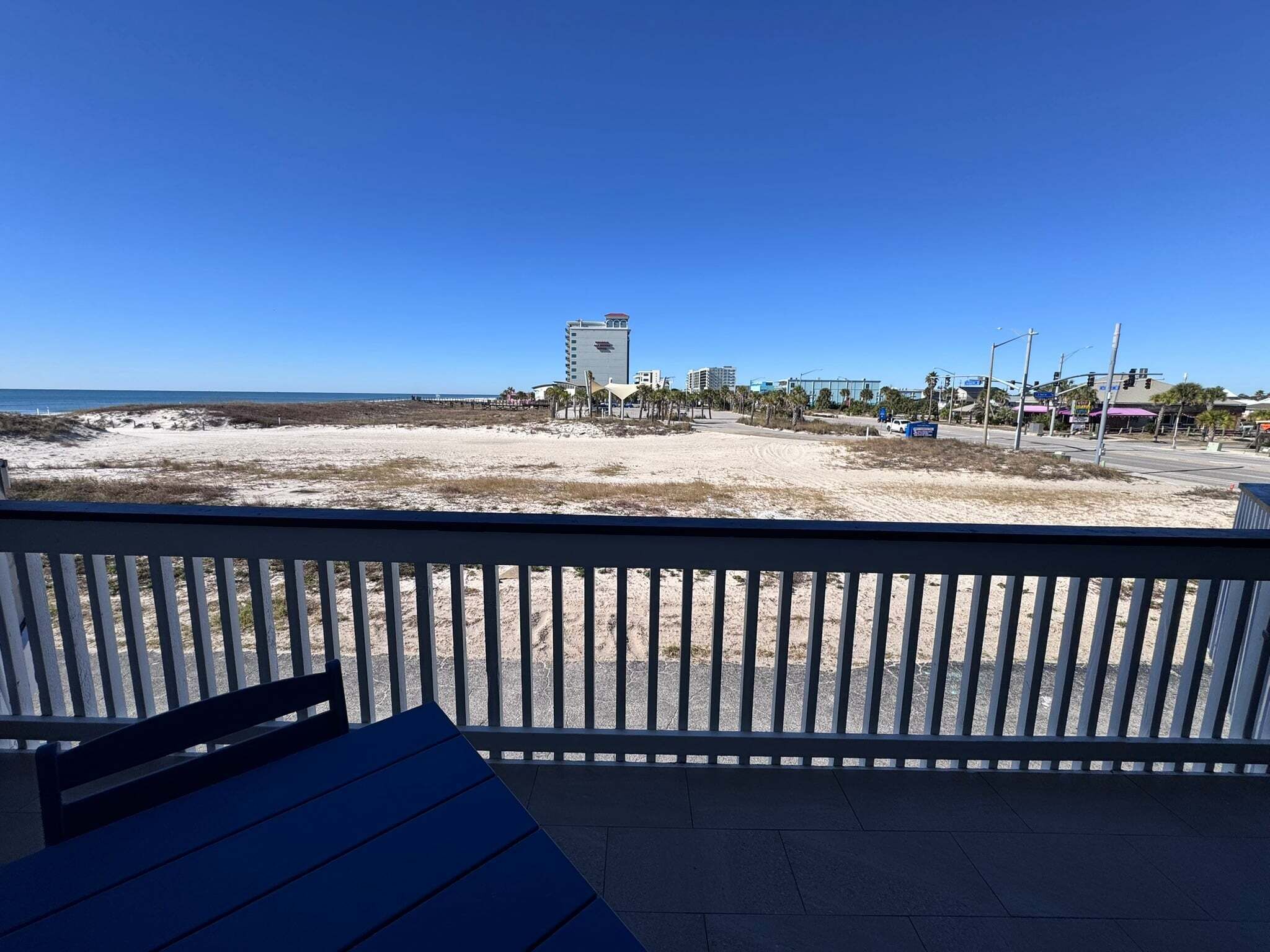 A beach view from a balcony with a railing, a table, and a chair.