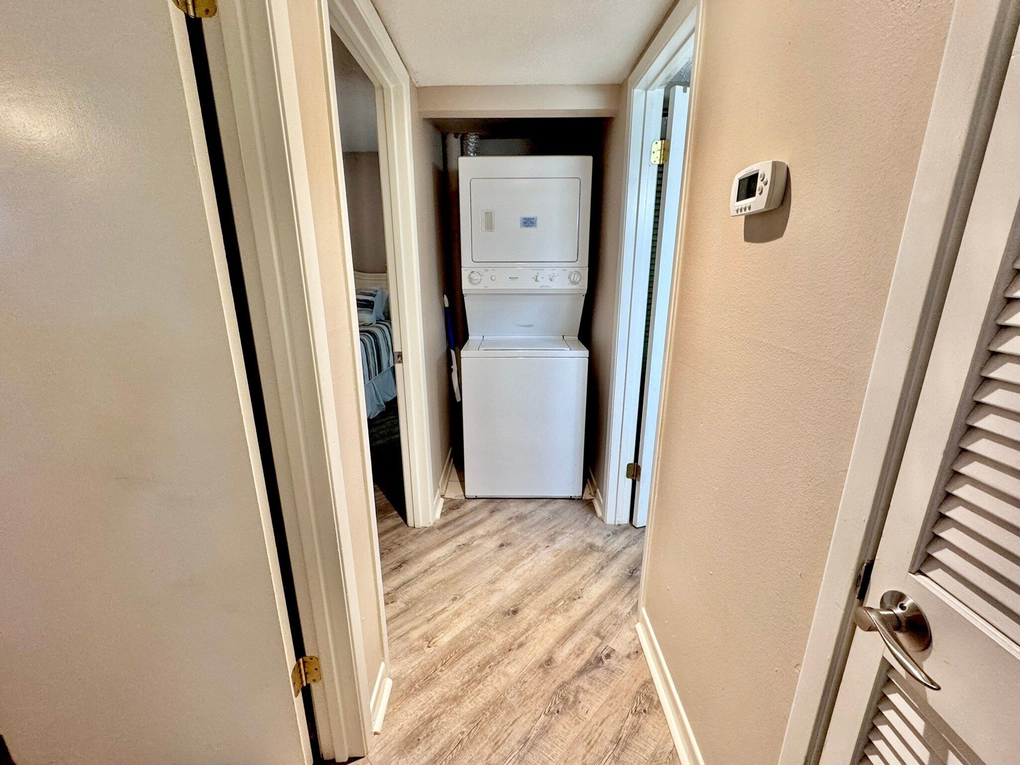 A narrow hallway with a wooden floor leading to a laundry area with a washer and dryer.