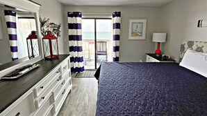 A bedroom with a bed, dresser, nightstand, lamp, and a view of the ocean through a balcony door. - Regatta (Gulf Shores)