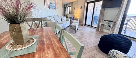 A spacious living area with a wooden dining table, a sofa, and a balcony with a view.