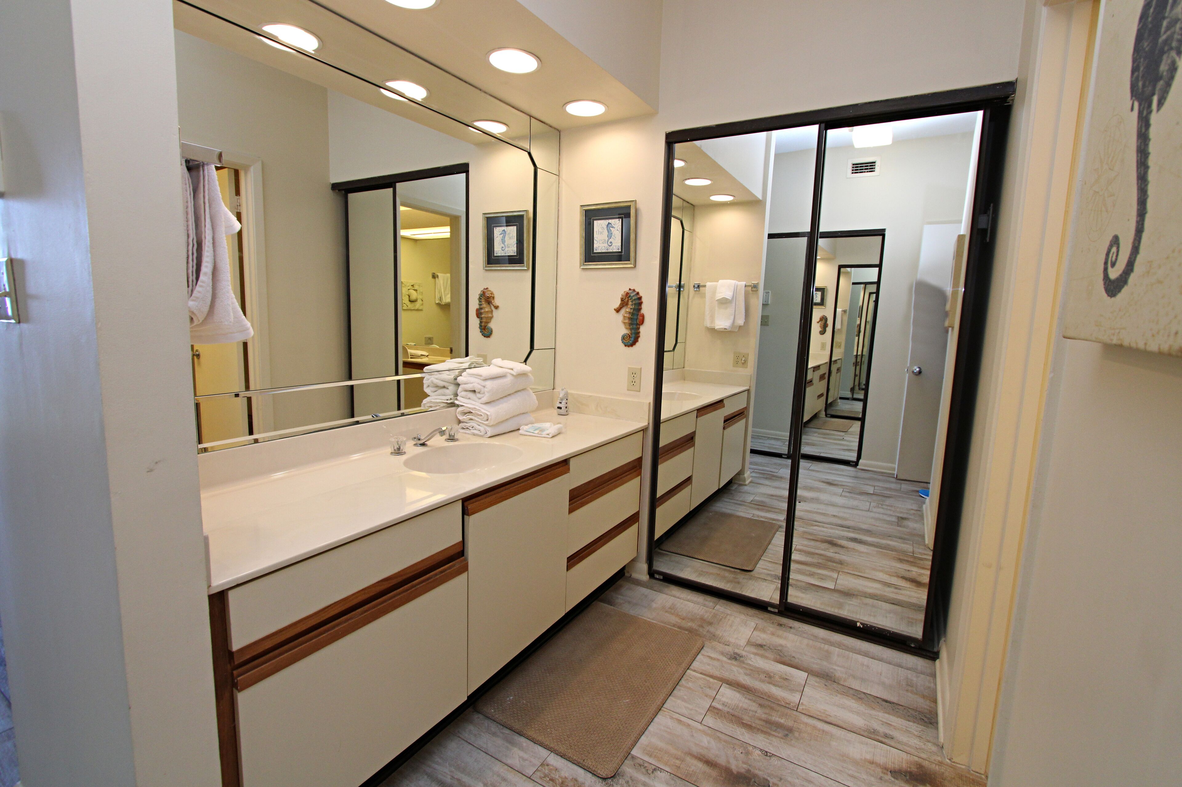 Un baño moderno con un espejo grande, encimeras blancas y detalles de madera.