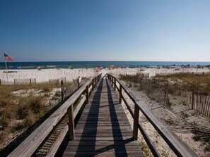 A wooden boardwalk leading to a sandy beach with umbrellas and beachgoers. - Romar Lakes (Orange Beach)