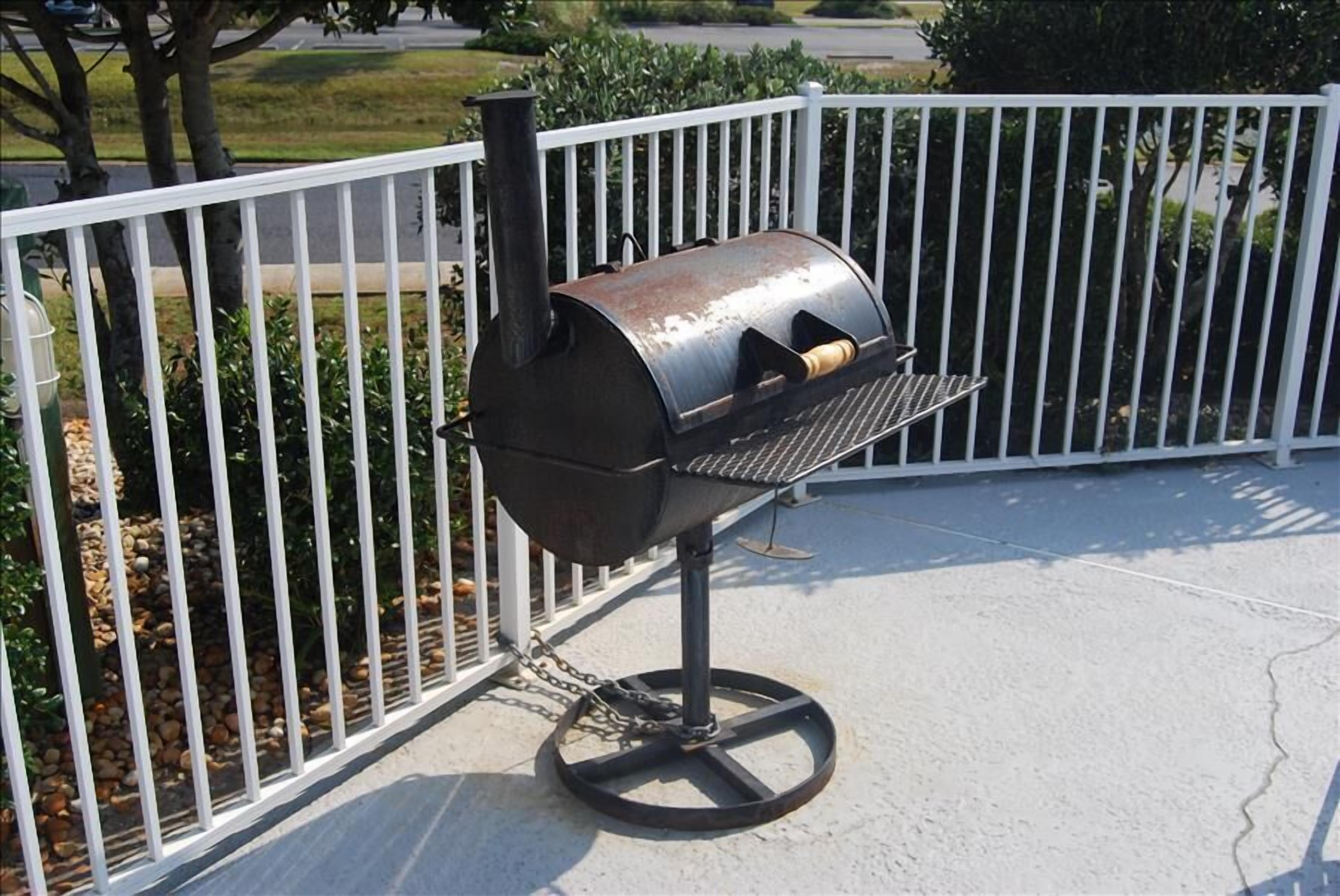 Un barbecue portable doté d’une cheminée en métal, placé sur une terrasse en béton, avec une clôture en métal blanche en arrière-plan.
