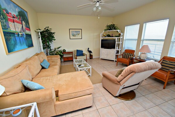 A living room with a beige sofa, a recliner, a coffee table, a TV stand, and a bookshelf. - Romar Lakes (Orange Beach)