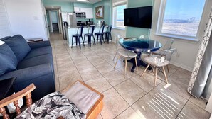 Un salon comprenant un canapé, une table basse, un coin repas avec des chaises, un téléviseur et une vue sur la plage.
