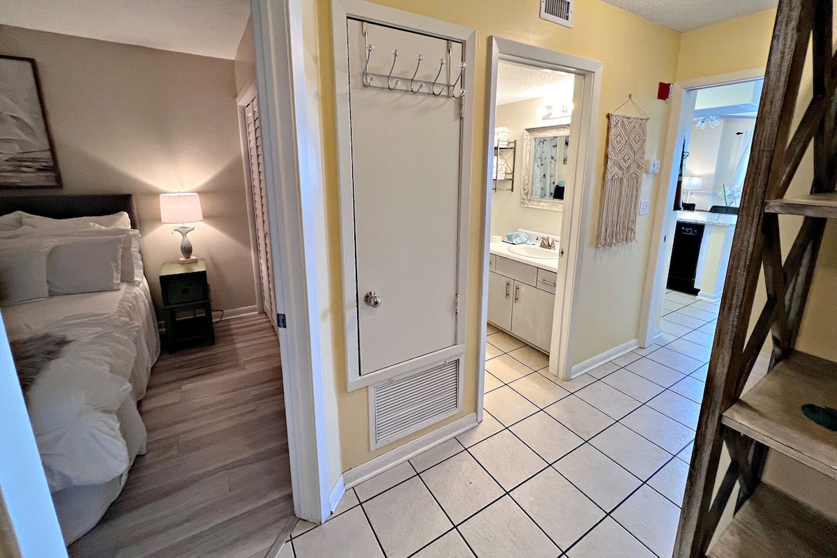 A hotel room with a bed, bedside table, lamp, and a bathroom visible through an open door.