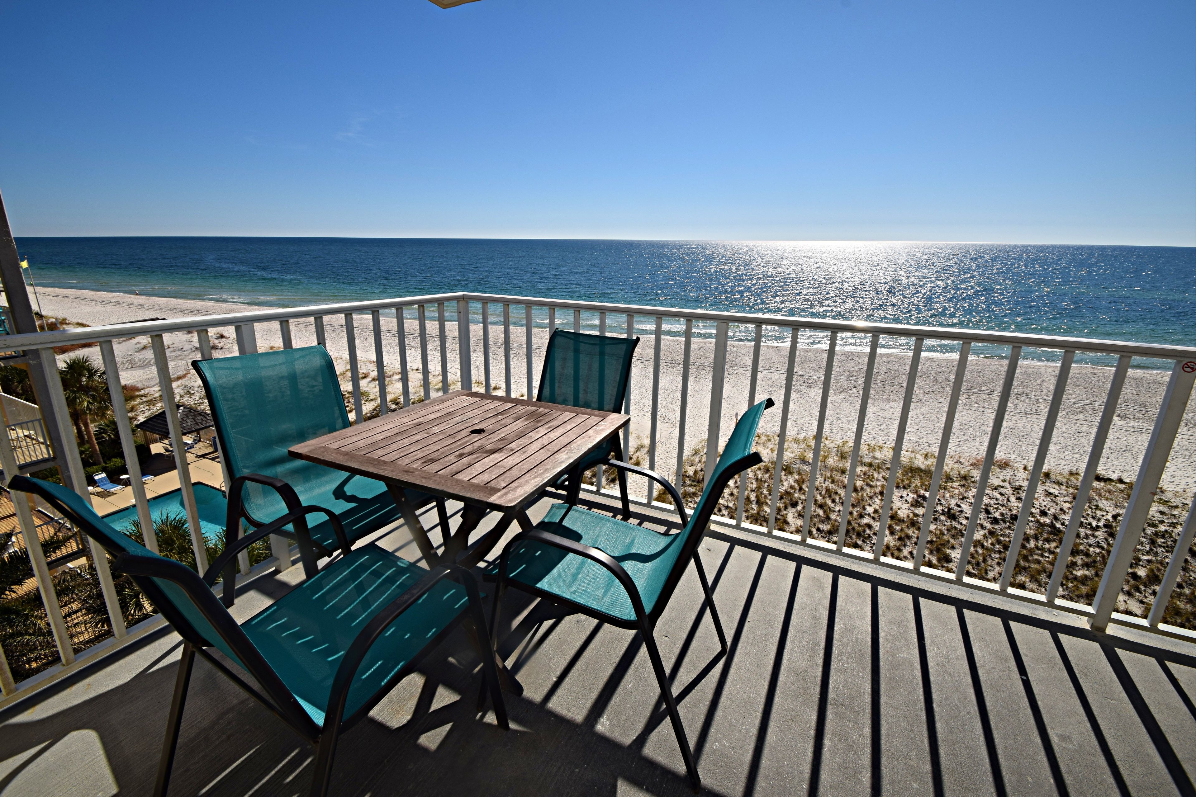 A wooden table with chairs on a balcony overlooking a beach.