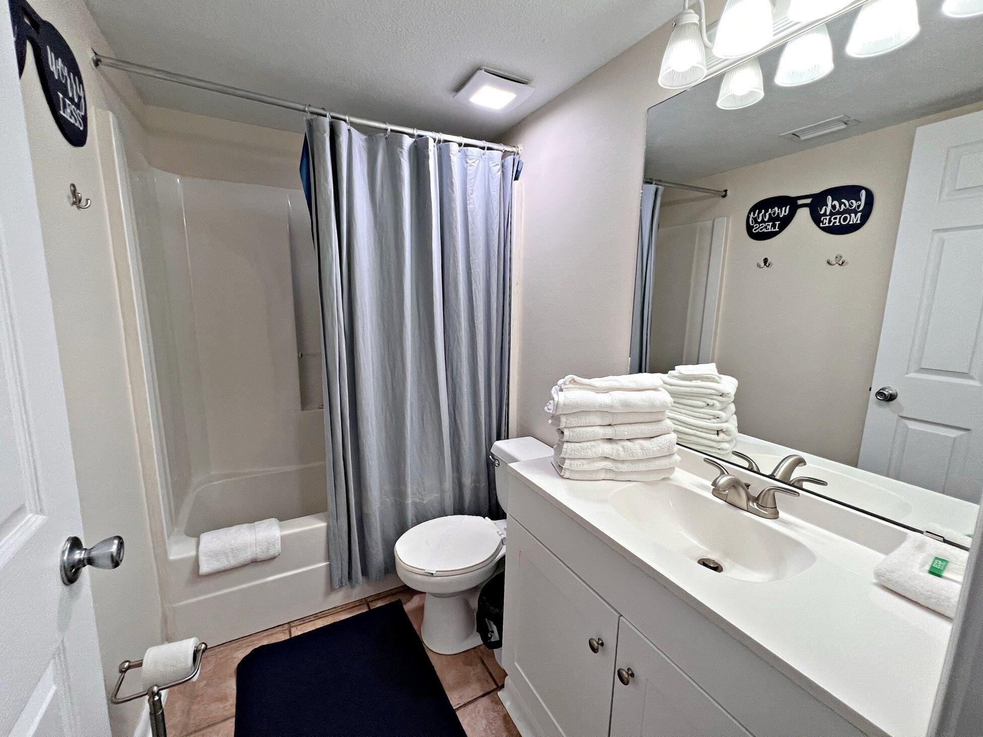 Une salle de bain avec une douche, des toilettes et un lavabo. Des serviettes sont pliées sur le lavabo et il y a un rideau de douche.