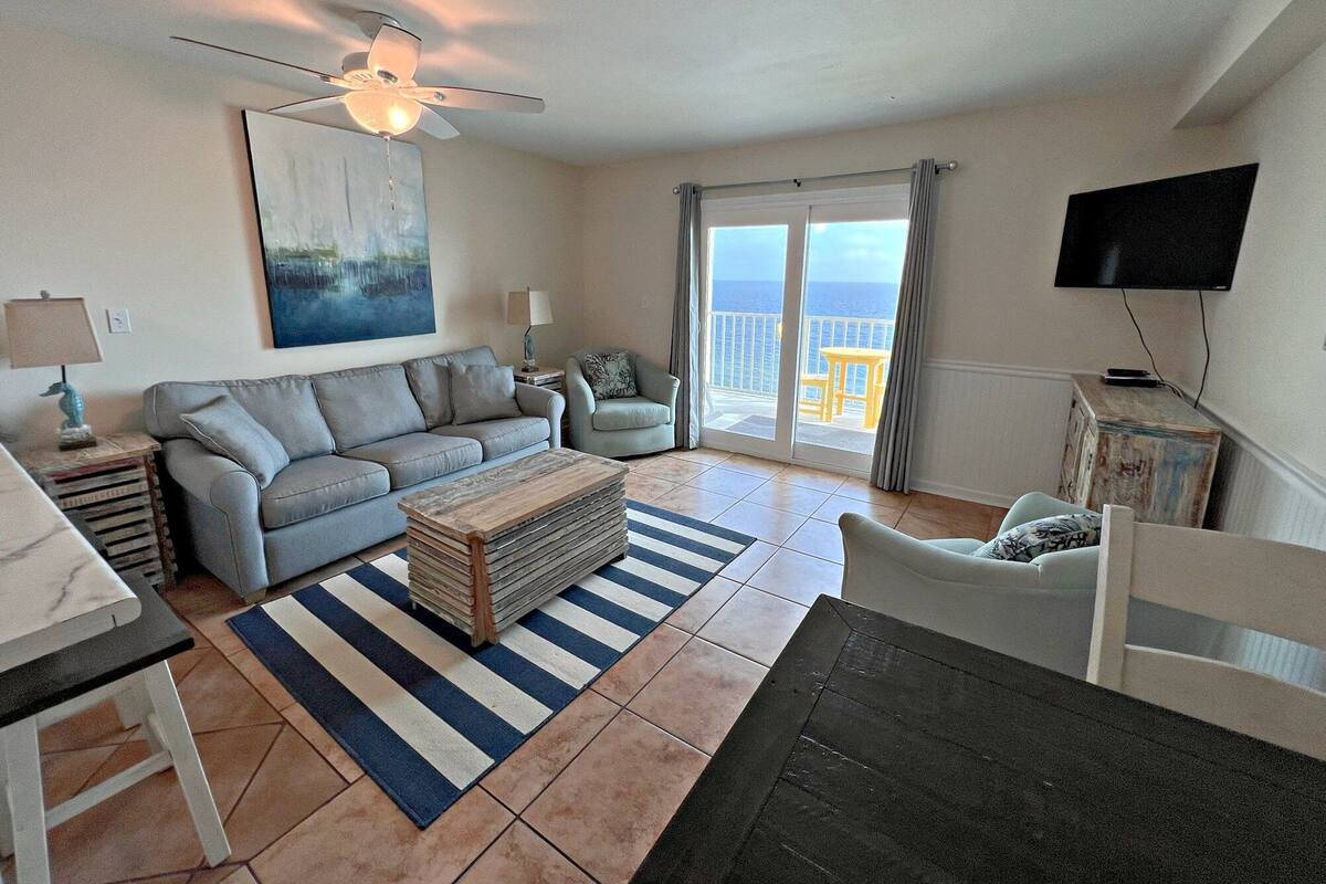 A living room with a sofa, a coffee table, a TV, and a balcony with a view.