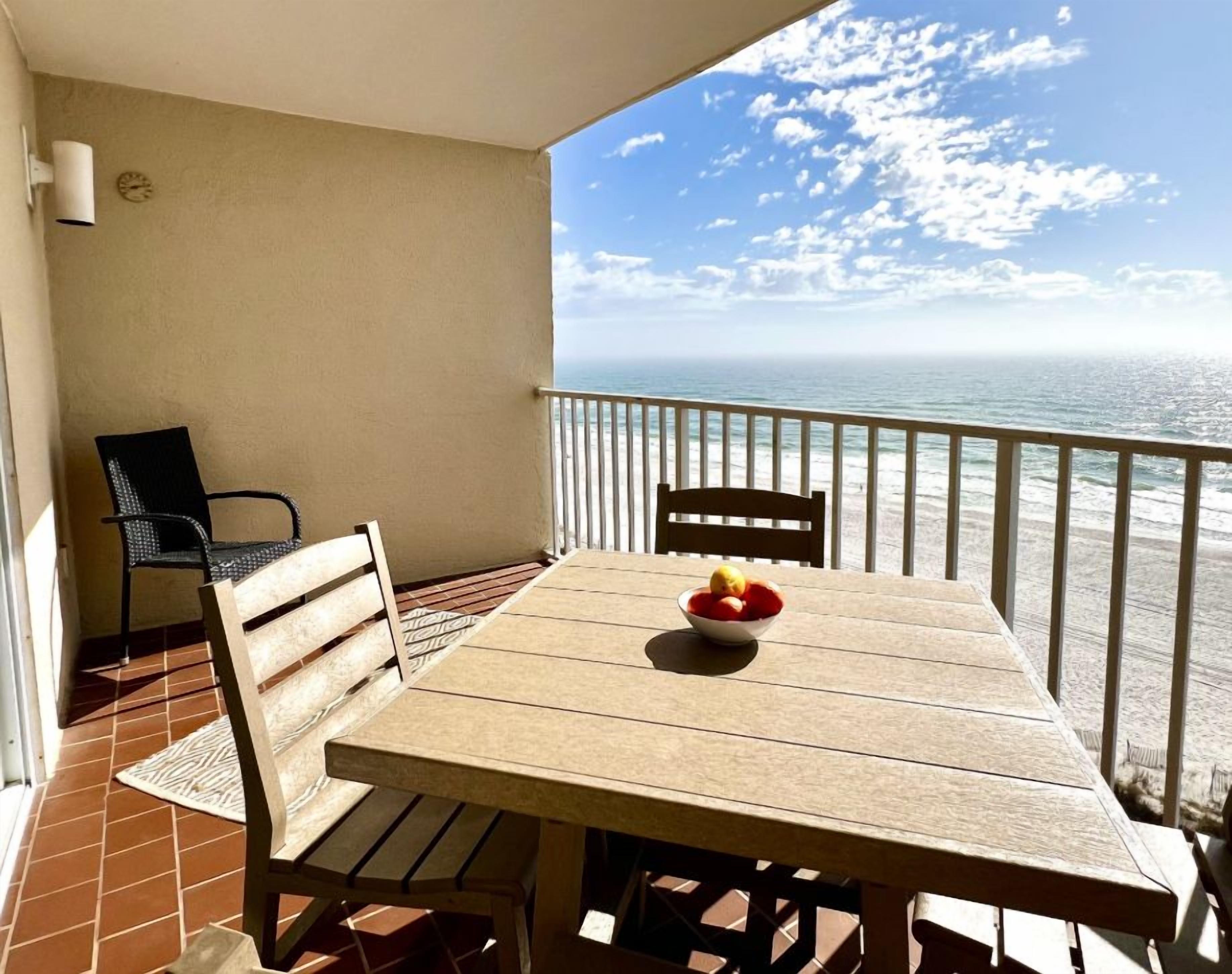 A wooden table with chairs on a balcony overlooking the ocean.