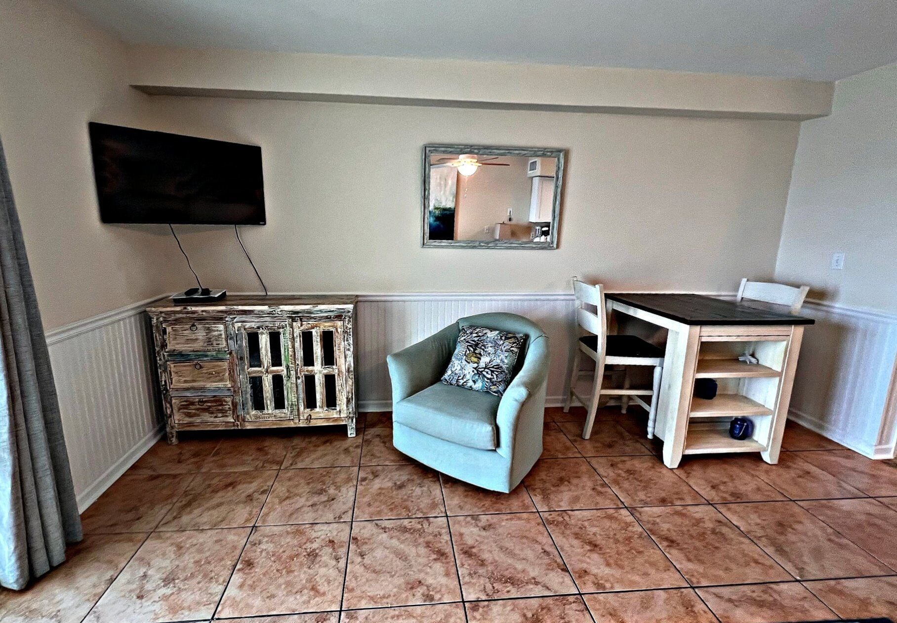 Uma sala de estar com televisão, uma cadeira, uma mesa e um armário.