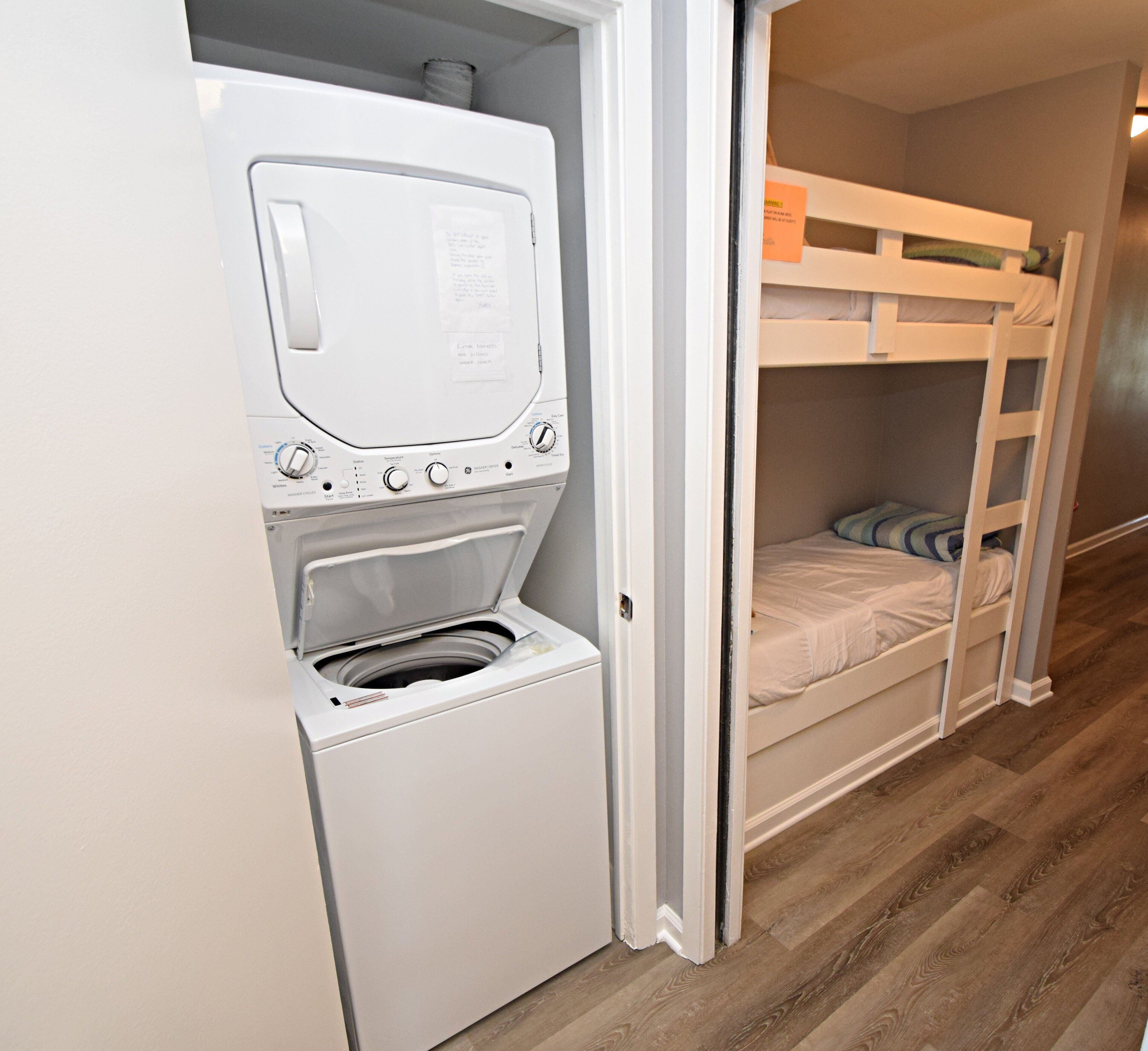 A laundry room with a washing machine and dryer, a bunk bed, and wooden flooring.