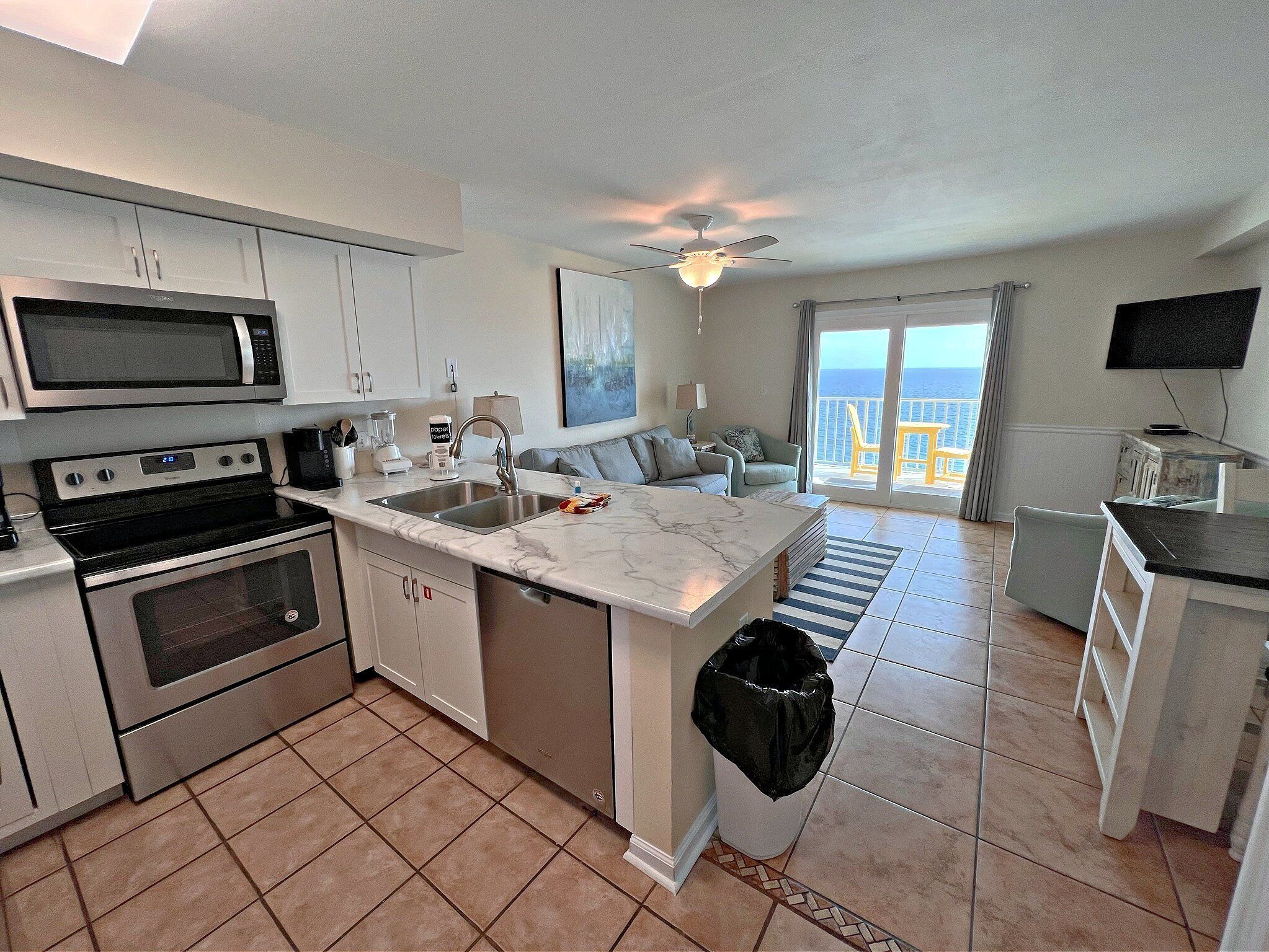 A modern kitchen with a central island, a dining area with a view, and a living room with a sofa and a TV.