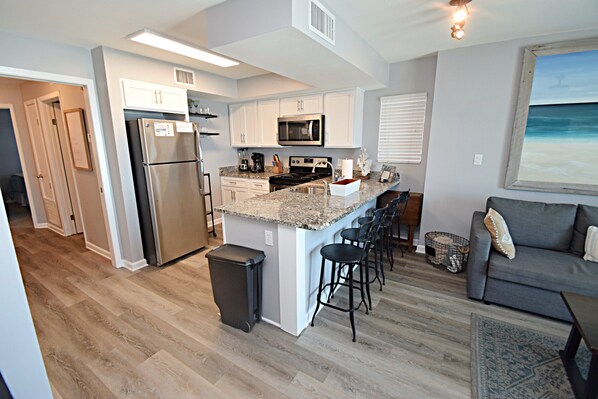 A modern kitchen with a central island, stainless steel appliances, and bar stools. - Seacrest (Gulf Shores)