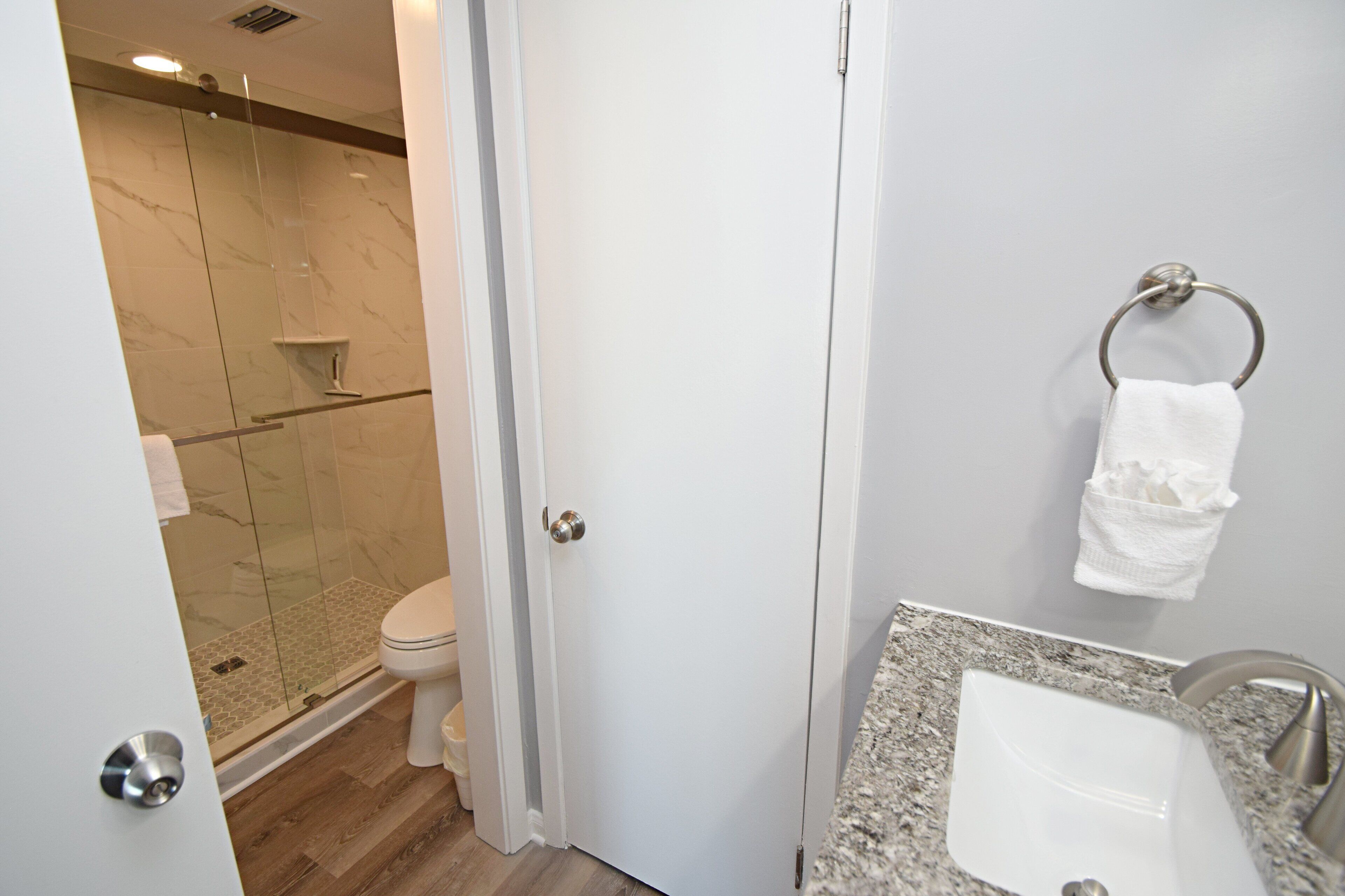 Un bagno moderno con cabina doccia in vetro, un water bianco, un piano di lavoro in granito e un lavandino.