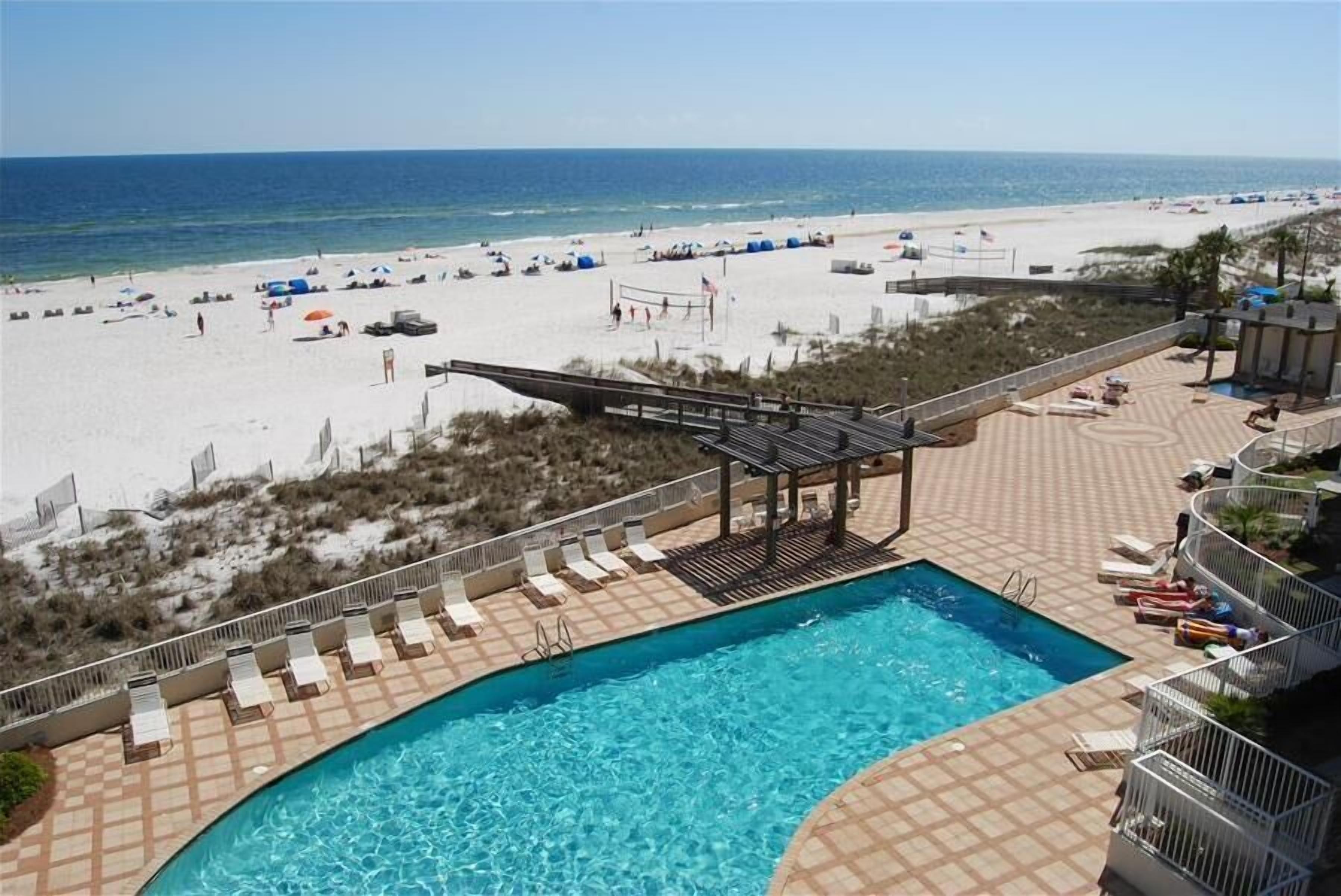 A pool area with a view of the beach, lounge chairs, and a covered seating area.