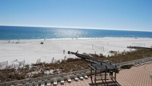 En strand med klar himmel, en sandstrand och en träpromenad som leder fram till strandstolar.