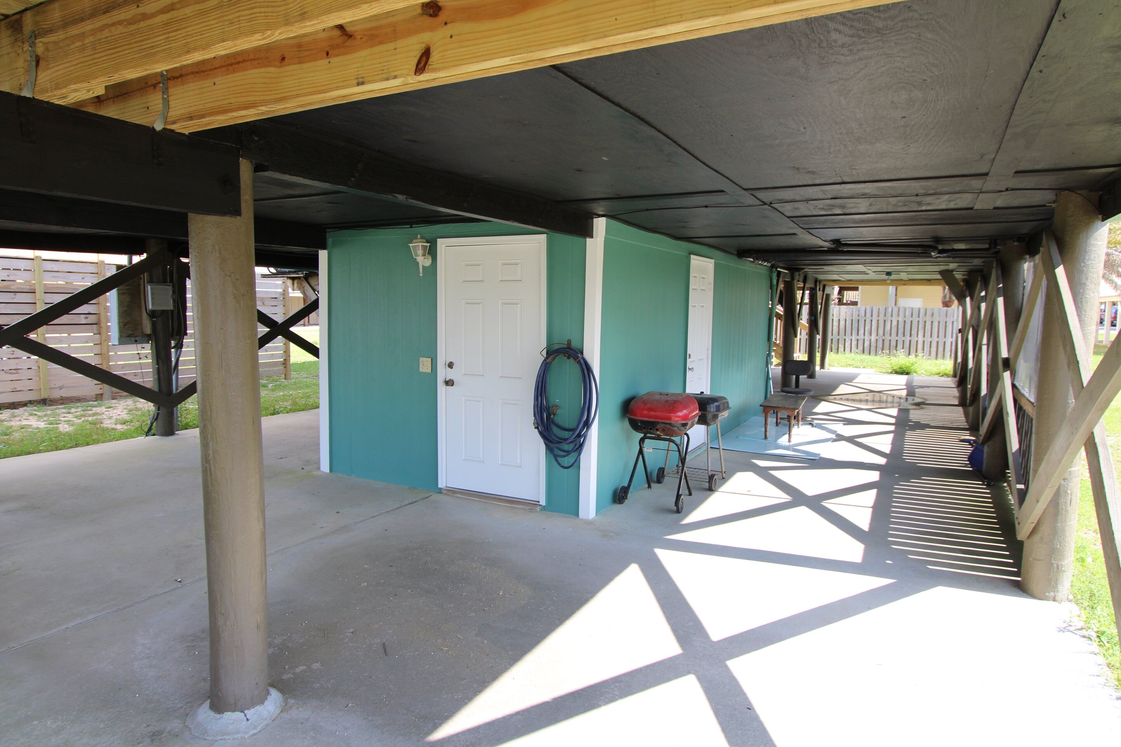 A covered outdoor area with a concrete floor, a door, and a hose coiled against the wall.