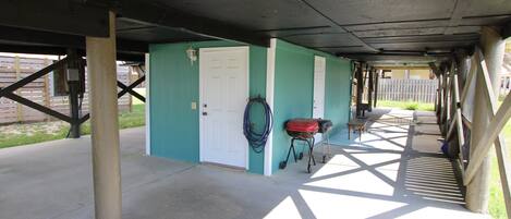 A covered outdoor area with a concrete floor, a door, and a hose coiled against the wall.