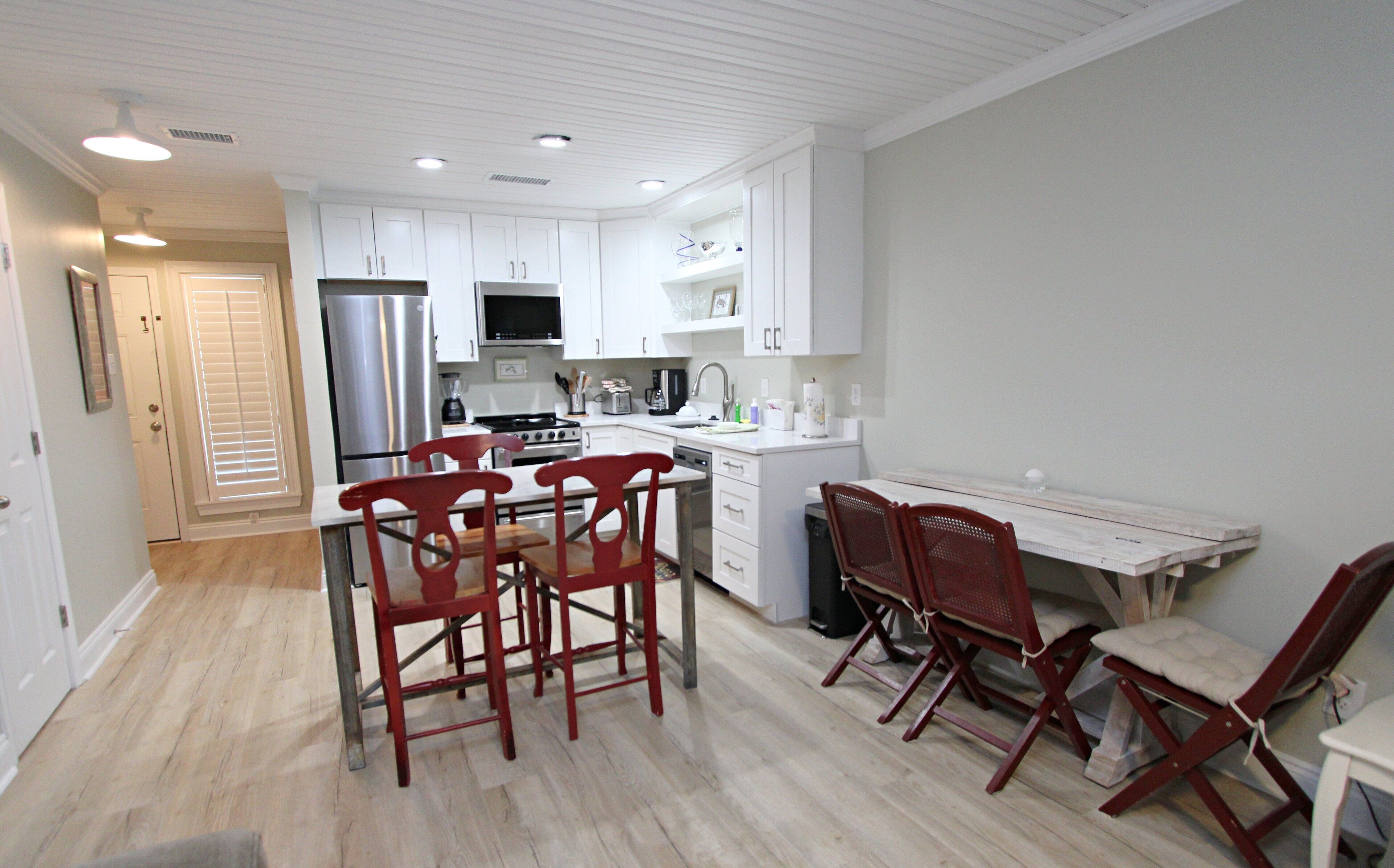 A modern kitchen with white cabinets, a stainless steel refrigerator, a microwave, and a stove. There is a dining area with a table and chairs.