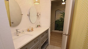 A bathroom with a white sink, two mirrors, a hairdryer, and a picture frame on the counter. - Southwinds (Gulf Shores)