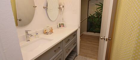 A bathroom with a white sink, two mirrors, a hairdryer, and a picture frame on the counter.