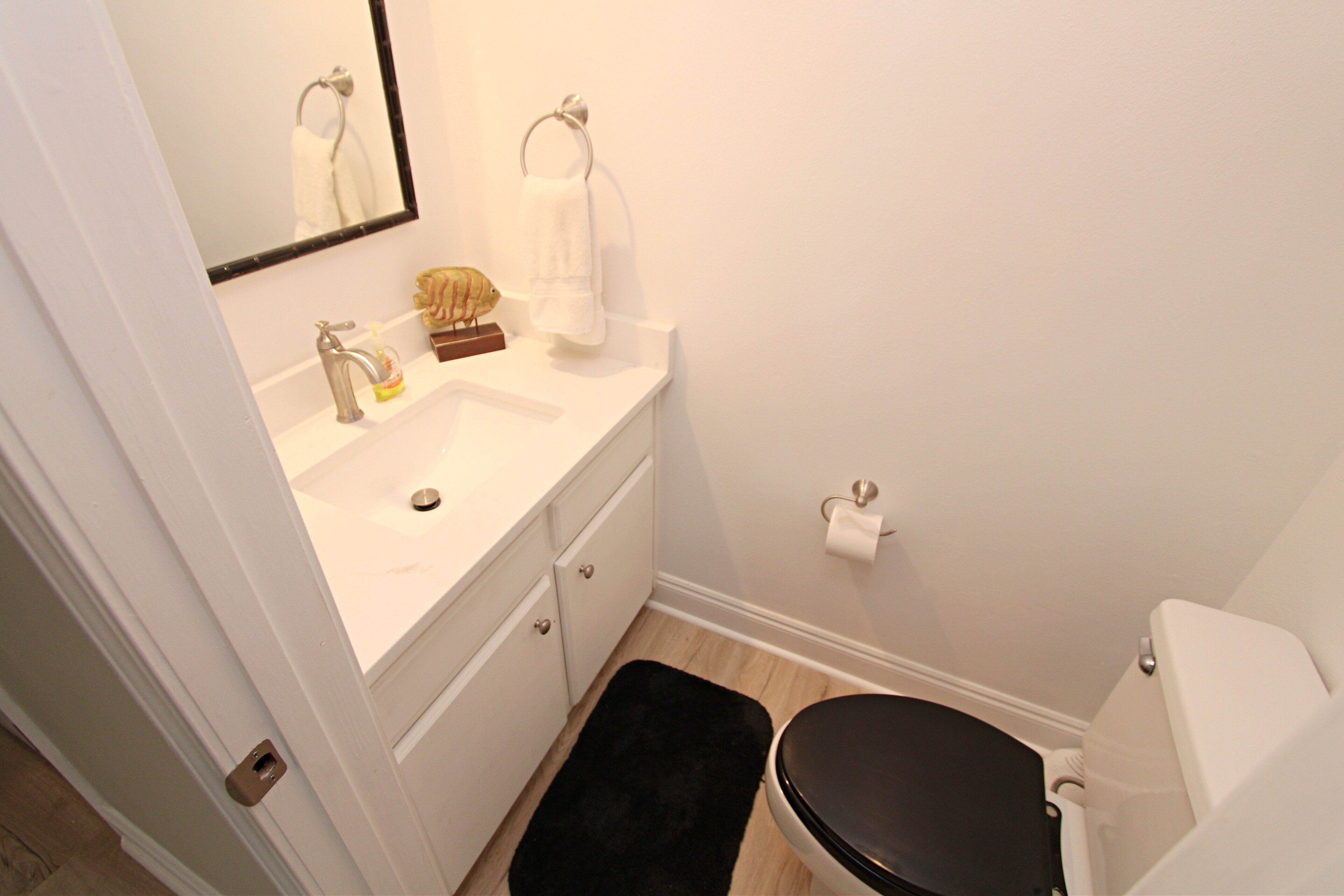 A bathroom with a white sink, a mirror, a toilet, and a black rug.